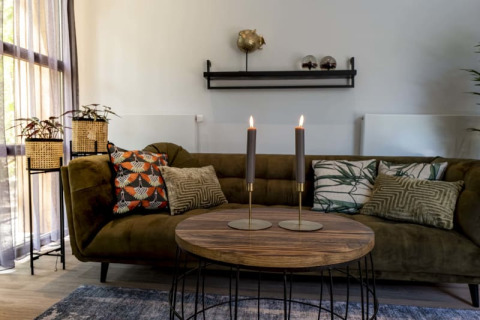 Accogliente soggiorno di lodge con divano verde, cuscini decorati, candele accese e piante in cesti.