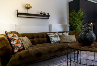 Sala moderna de lodge con sofá verde, cojines decorativos, mesa redonda y planta grande en la esquina.