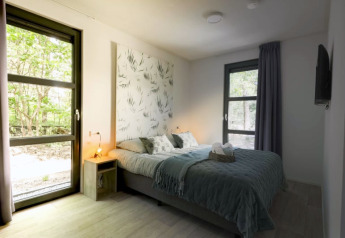Chambre moderne de lodge avec lit double, grandes fenêtres, lumière naturelle et vue sur la nature.