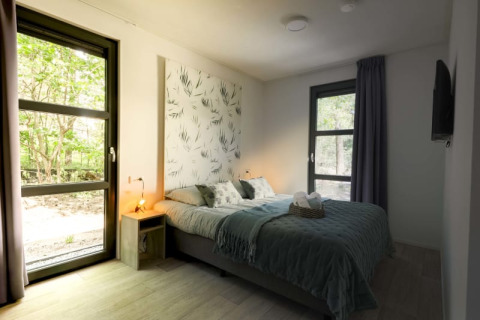 Modernes Schlafzimmer in einer Lodge mit Doppelbett, großen Fenstern, Tageslicht und Naturblick.