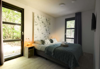 Modernes Schlafzimmer in einer Lodge mit Doppelbett, großen Fenstern, Tageslicht und Naturblick.