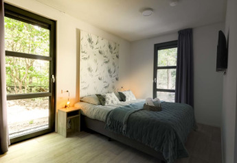 Moderne lodge slaapkamer met tweepersoonsbed, grote ramen, veel daglicht en uitzicht op het groen.