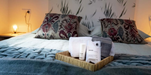 Gemütliches Lodge-Zimmer mit gemachtem Bett, dekorativen Kissen und einem Willkommensset auf einer Bambusablage.