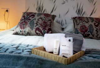 Et hyggeligt lodgeværelse med seng, bløde puder, natbordslamper og en bakke med toiletartikler på sengen.