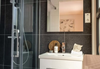 Salle de bain moderne dans un lodge avec douche vitrée, carrelage foncé, meuble blanc et miroir mural.