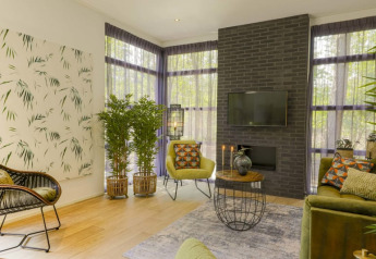 Modern lodge living room with lush plants, stylish furniture, black brick wall, and large curtained windows.