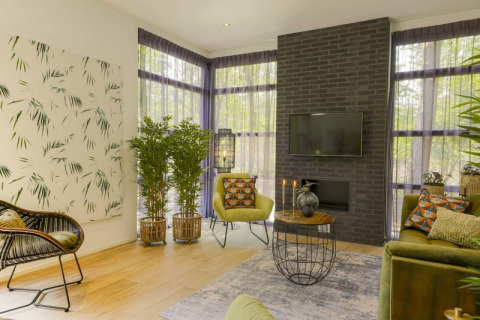 Salón de lodge moderno con plantas verdes, muebles elegantes, una pared de ladrillo negra y grandes ventanas.