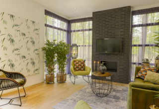 Salón de lodge moderno con plantas verdes, muebles elegantes, una pared de ladrillo negra y grandes ventanas.