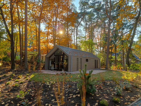 Una moderna casa lodge enclavada en un bosque otoñal, rodeada de árboles coloridos y luz solar.