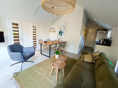 Salón de lodge moderno con sofá verde, sillón gris, mesas de madera, mesa de comedor y luz natural.