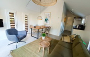 Salón de lodge moderno con sofá verde, sillón gris, mesas de madera, mesa de comedor y luz natural.