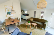 Interior de lodge moderno con área de estar abierta, sofá verde, mesa de comedor y lámparas de mimbre.