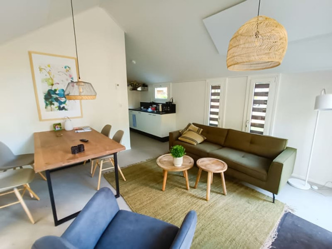 Interior de lodge moderno con área de estar abierta, sofá verde, mesa de comedor y lámparas de mimbre.