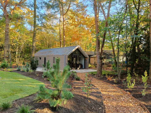 Een moderne lodge in een bosrijke omgeving, met een houtsnipperpad naar de voordeur op een zonnige dag.
