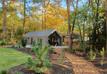 Un lodge moderne entouré d’arbres, avec un sentier de copeaux menant vers l’entrée, par une journée ensoleillée.