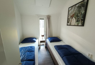 Habitación acogedora en un albergue con dos camas individuales, ropa de cama azul, ventana y cuadro.