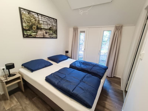 Dormitorio luminoso de cabaña con dos camas individuales, ropa de cama azul y ventanales con vista al bosque.