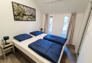 Dormitorio luminoso de cabaña con dos camas individuales, ropa de cama azul y ventanales con vista al bosque.