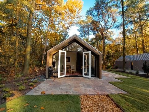 Foto de una moderna cabaña en el bosque con puertas dobles abiertas y hojas de otoño sobre el césped.
