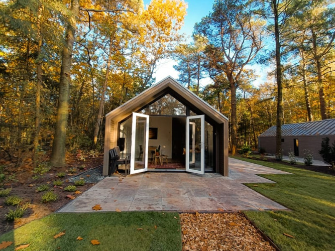 Foto de una moderna cabaña en el bosque con puertas dobles abiertas y hojas de otoño sobre el césped.