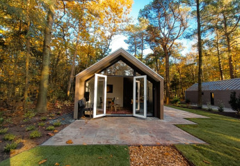 Foto de una moderna cabaña en el bosque con puertas dobles abiertas y hojas de otoño sobre el césped.