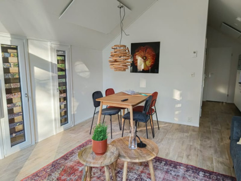 Intérieur lumineux de lodge avec table, quatre chaises, tapis coloré, suspension moderne et art mural.