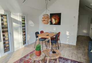 Intérieur lumineux de lodge avec table, quatre chaises, tapis coloré, suspension moderne et art mural.