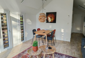 Intérieur lumineux de lodge avec table, quatre chaises, tapis coloré, suspension moderne et art mural.