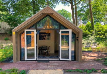 Foto di un'accogliente lodge con porte aperte, immersa nel verde tra alberi e natura rigogliosa.