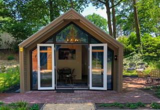 Foto van een gezellige lodge met open deuren, omgeven door prachtig groen en bomen in een bosrijke omgeving.