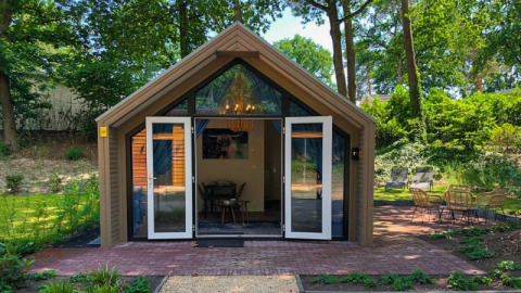 Foto van een gezellige lodge met open deuren, omgeven door prachtig groen en bomen in een bosrijke omgeving.