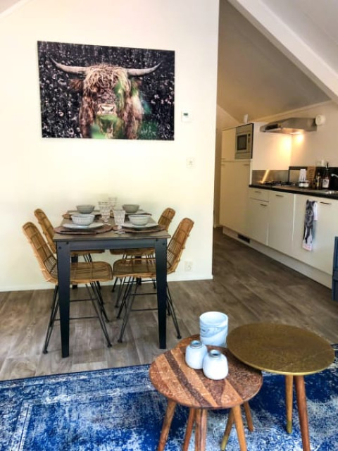Salle à manger d'un lodge avec quatre chaises, cuisine moderne et grande peinture de vache au mur.