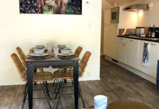 Comedor en una cabaña con cuatro sillas, cocina moderna y un gran cuadro de vaca en la pared.