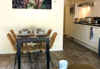 Salle à manger d'un lodge avec quatre chaises, cuisine moderne et grande peinture de vache au mur.