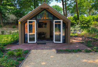 Moderne lodge met glazen deuren, een bakstenen terras en een zithoek, omgeven door groene natuur.