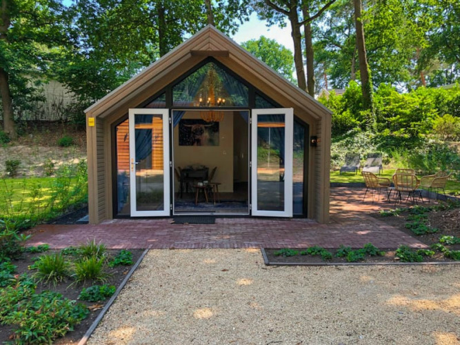 Moderne Lodge mit Glasfassade und Terrassenbereich im Wald, gemütliche Sitzgelegenheiten im Freien.