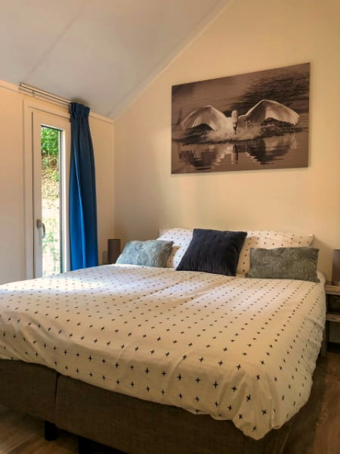 Chambre douillette dans un lodge avec grand lit, rideaux bleus et tableau de cygne au-dessus du lit.