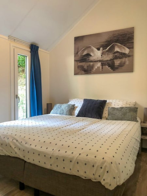 Acogedor dormitorio en un lodge con cama grande, cortinas azules y un cuadro de cisne sobre la cama.