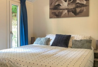 Gezellige slaapkamer in een lodge met groot bed, blauwe gordijnen en een schilderij van een zwaan boven het bed.