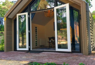 Lodge moderno con puertas de cristal abiertas, detalles de madera y pequeño jardín, rodeado de árboles.