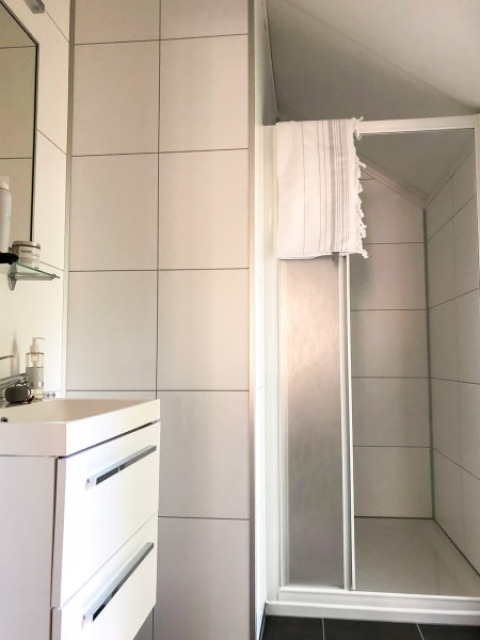 Baño moderno en una cabaña con azulejos blancos, lavabo, espejo y una ducha con toalla colgada.