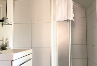 Baño moderno en una cabaña con azulejos blancos, lavabo, espejo y una ducha con toalla colgada.