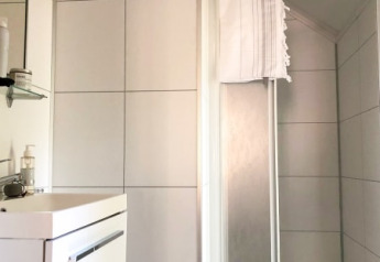 Moderne badeværelse i et lodge med hvidt flisegulv, håndvask, spejl og bruseniche med håndklæde.