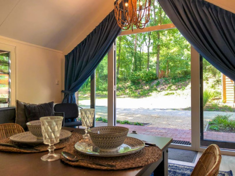 Sala da pranzo in un lodge con stoviglie eleganti, porte di vetro aperte e vista su una foresta verde.