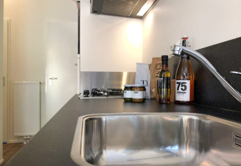 Et moderne køkken i en lodge med vask, armatur, køkkenbord og flasker samt krukker med madvarer.