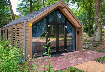 Un moderno lodge in legno con grandi porte di vetro, immerso nel verde e circondato da alberi.