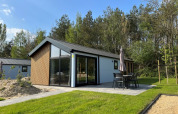 Lodge moderne avec grandes baies vitrées, terrasse avec mobilier et parasol, entouré de pelouse et d’arbres.