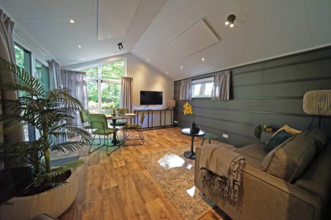 Moderne lodgewoonkamer met groene stoelen, groot raam, houten vloer en gezellige planten.