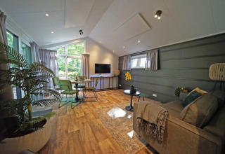 Moderne lodgewoonkamer met groene stoelen, groot raam, houten vloer en gezellige planten.