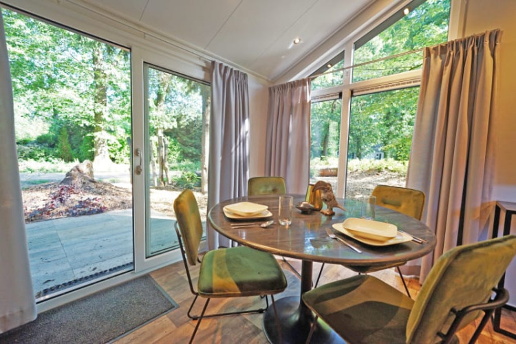 Heller Essbereich in einer Lodge mit vier Stühlen, großem Fenster und Blick auf den grünen Wald draußen.